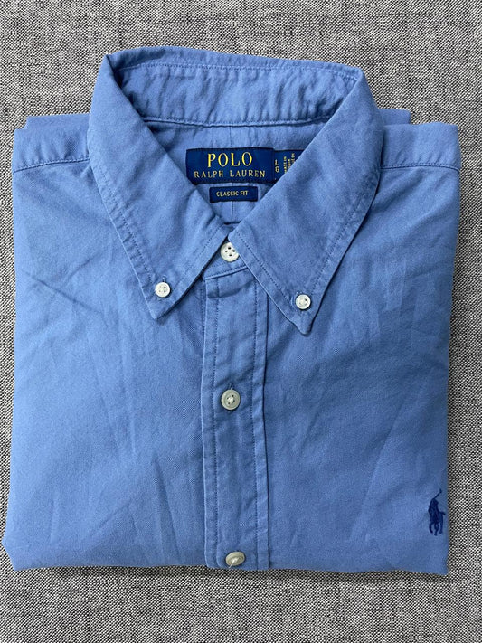 Folded blue Polo Ralph Lauren shirt on a textured gray surface